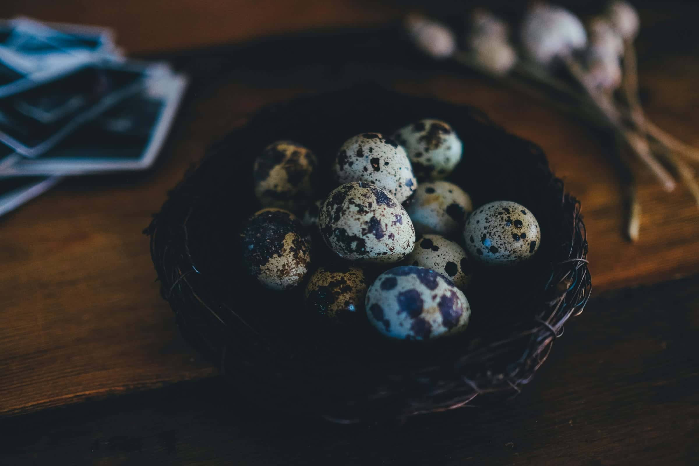 Telur puyuh berbintik di dalam sarang anyaman gelap di atas meja kayu