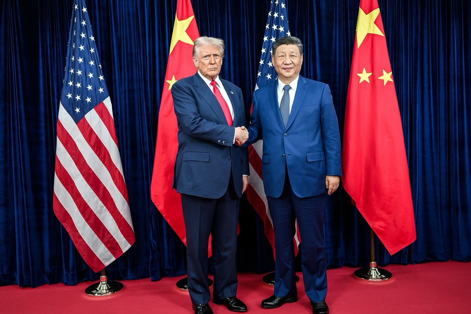 Presiden AS Donald Trump dan Presiden Tiongkok Xi Jinping berjabat tangan di depan bendera kedua negara, pada pertemuan 2025 di Korea Selatan