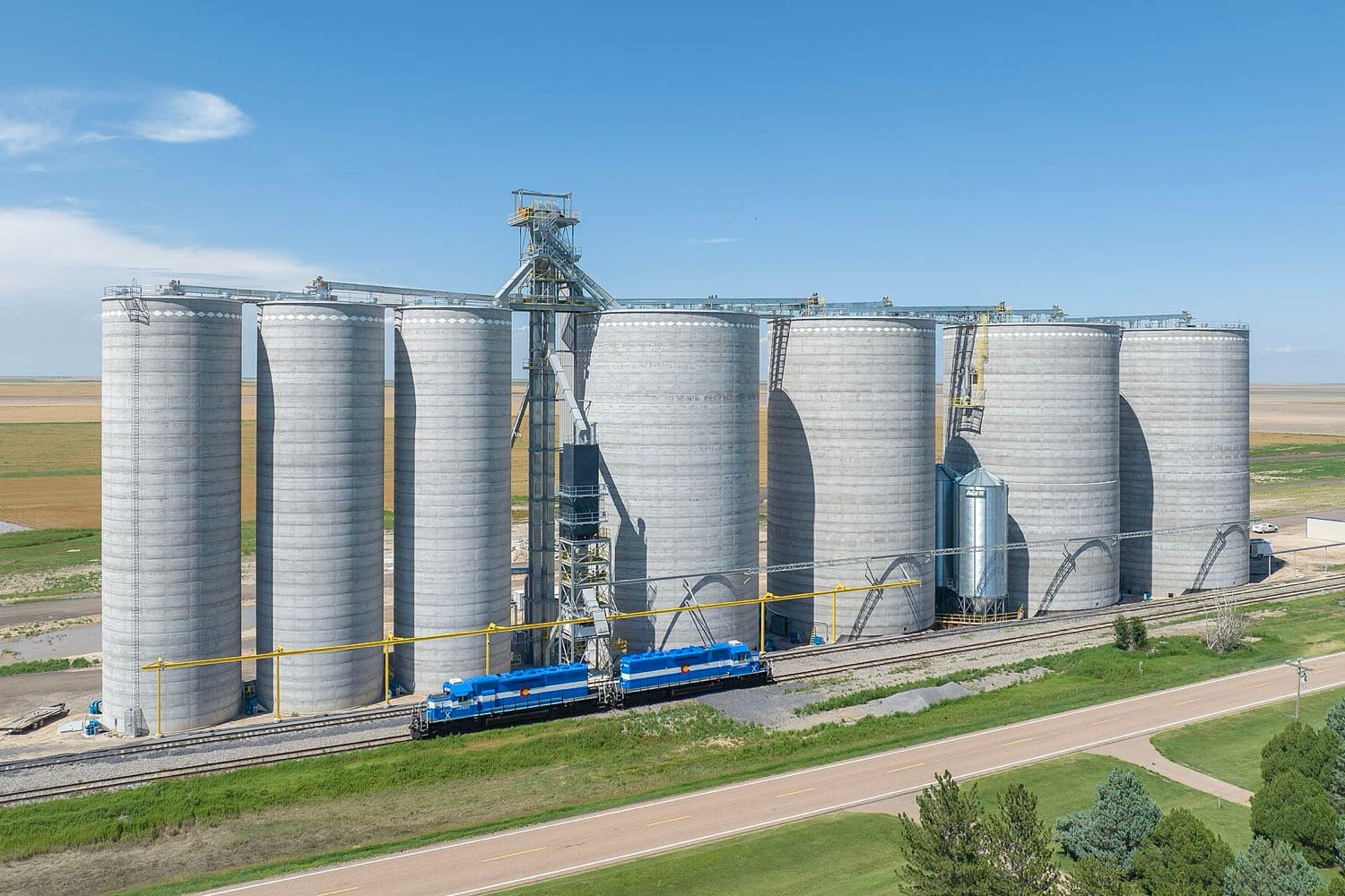 Deretan silo biji-bijian beton di dataran Colorado, Amerika Serikat, dengan lokomotif biru di depannya