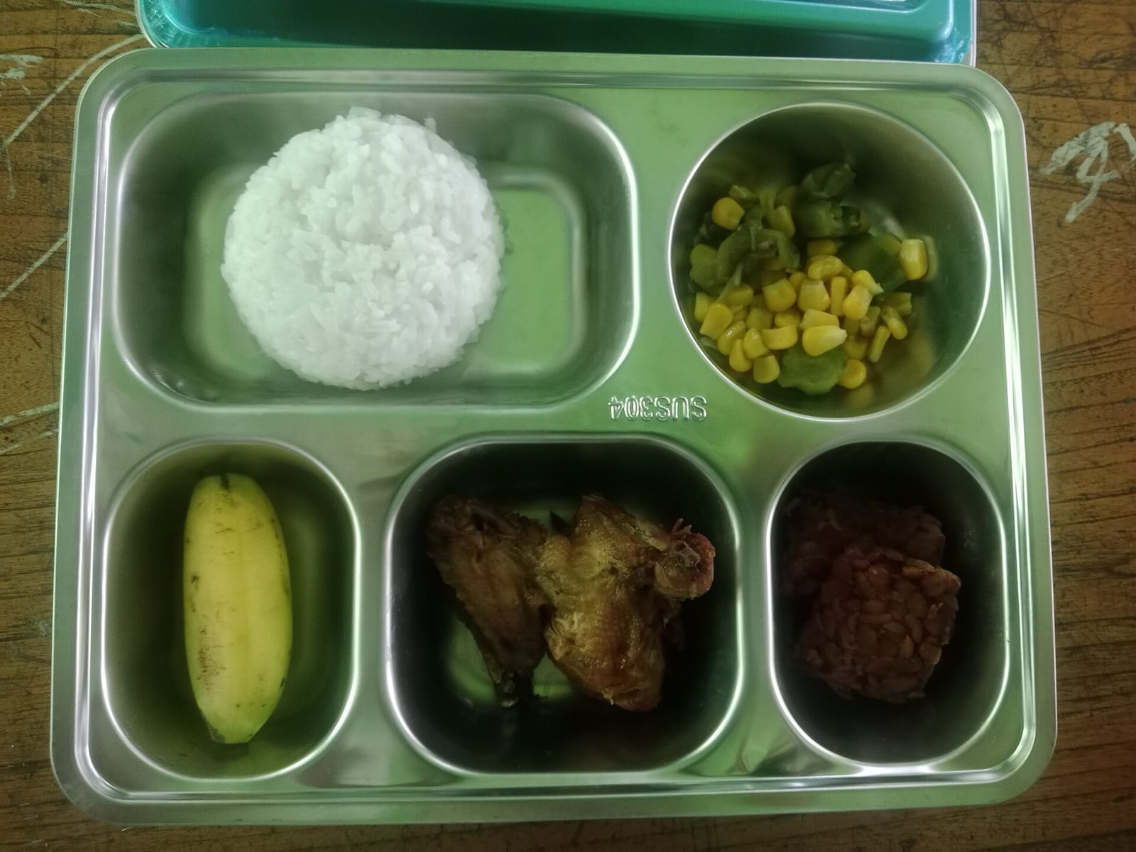 Ompreng stainless berisi nasi, jagung manis, pisang, dan lauk dari program Makan Bergizi Gratis di sebuah SMP