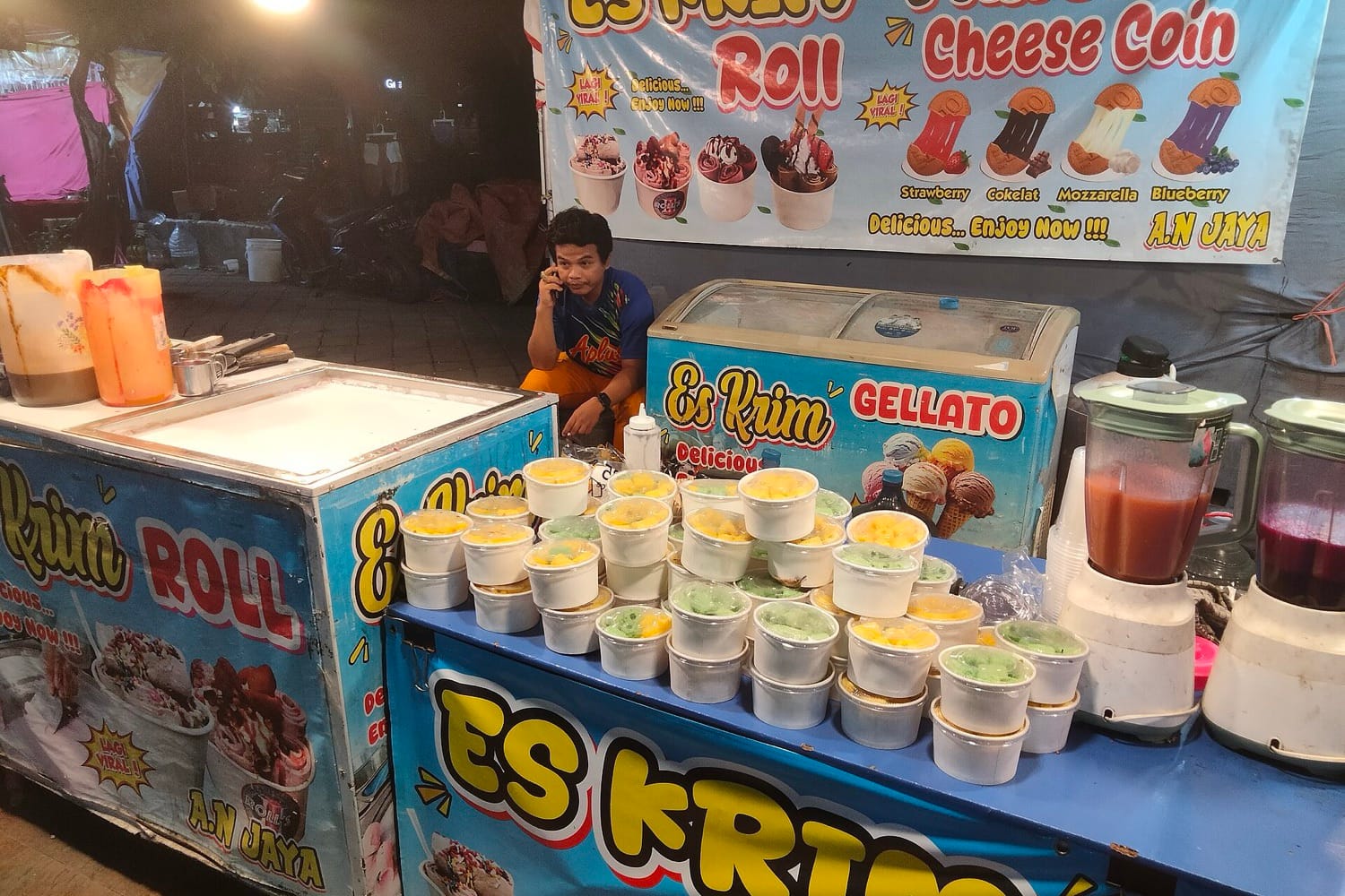 Lapak pedagang es krim gulung malam hari di Pasar Malam Ngawi, dengan penjual duduk di balik gerobak
